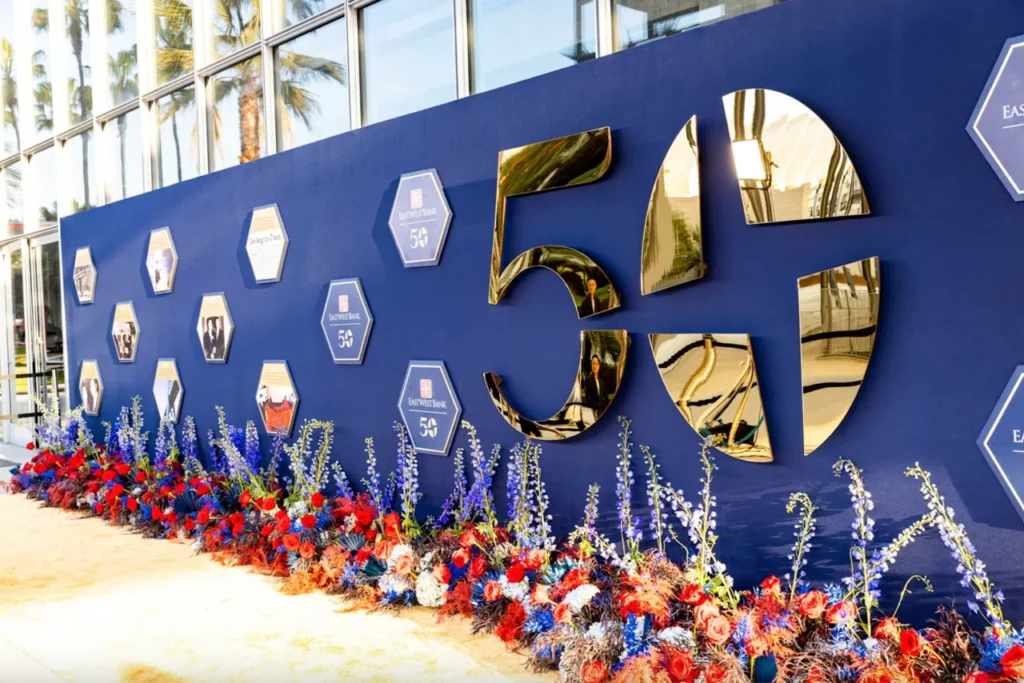 Elegant 50th anniversary corporate event wall branding with blue backdrop and red floral arrangements.