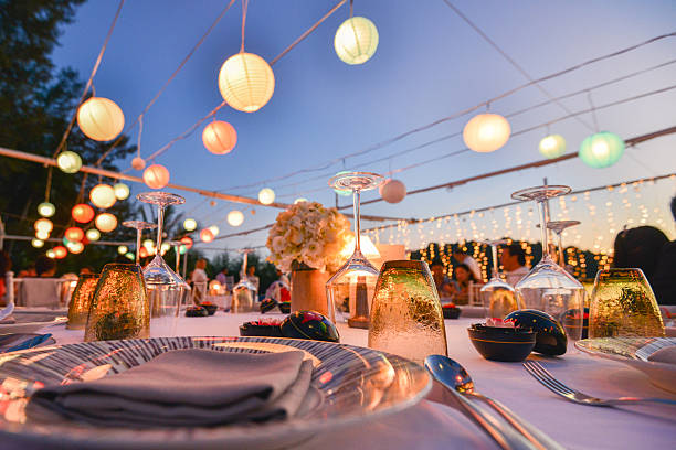 Beautiful outdoor wedding reception setup with glowing lanterns and decorated dinner table at sunset.